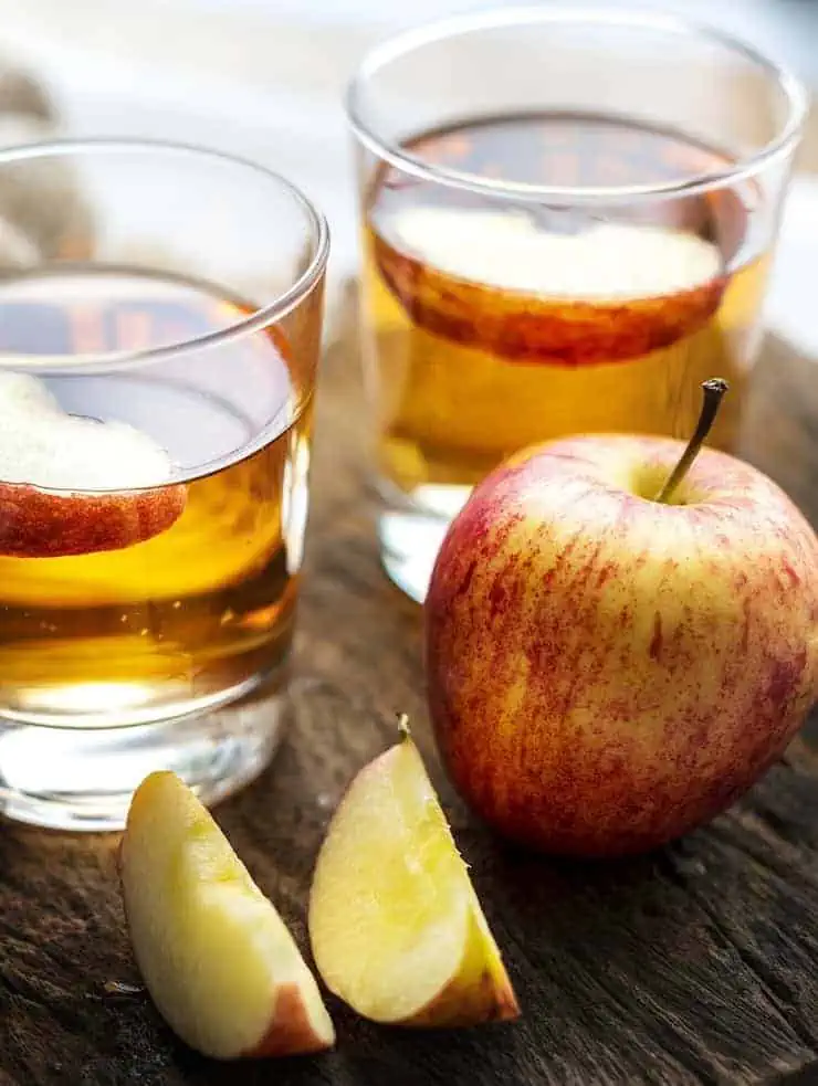 Glass of apple cider with slices of apple in it on wooden table