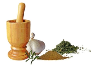Wooden mortar and pestle next to garlic and herbs