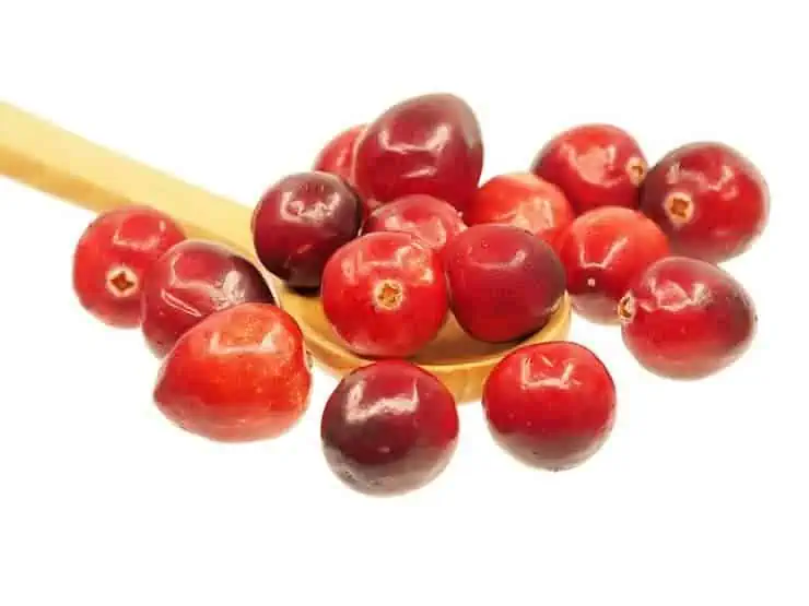 Red cranberries on a wooden spoon on a white surface