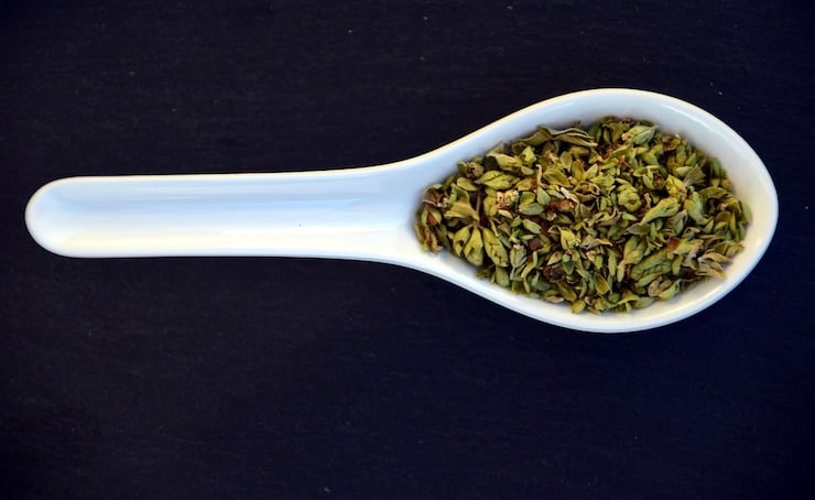 White ceramic spoon filled with green oregano on a black surface