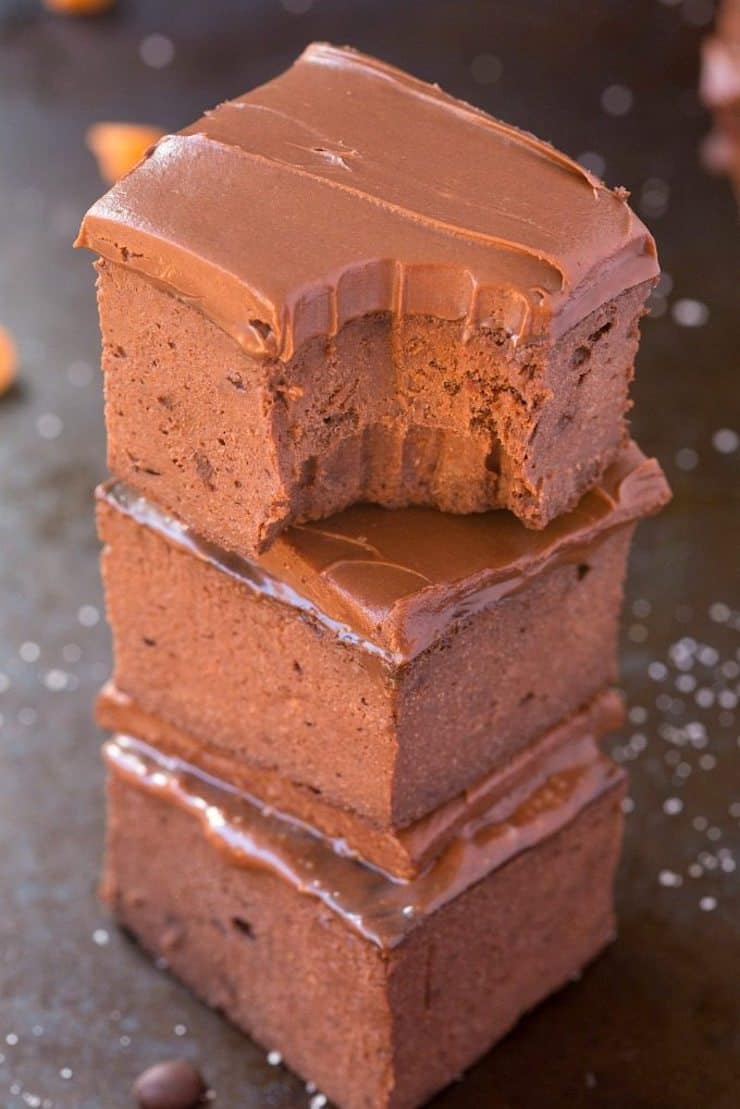 three stacked frosted brownies on a grey sheet