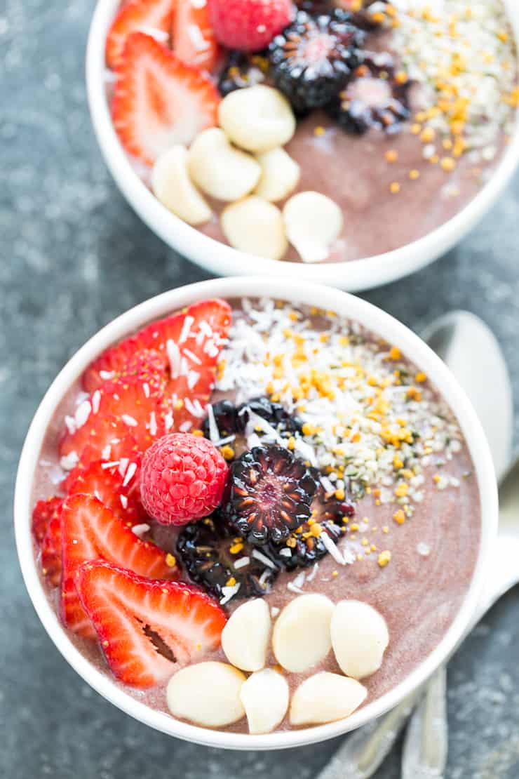 Smoothie in white bowl topped with berries, nuts and shredded coconut
