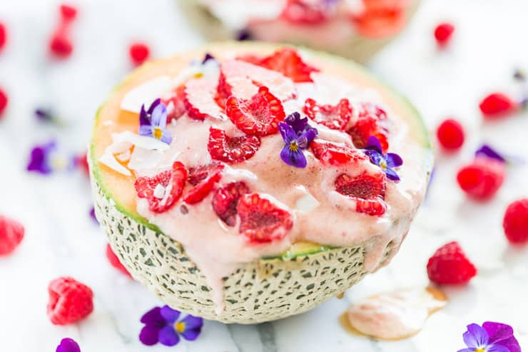Halved cantaloupe with ice cream in the middle topped with raspberries and purple flowers spilling out