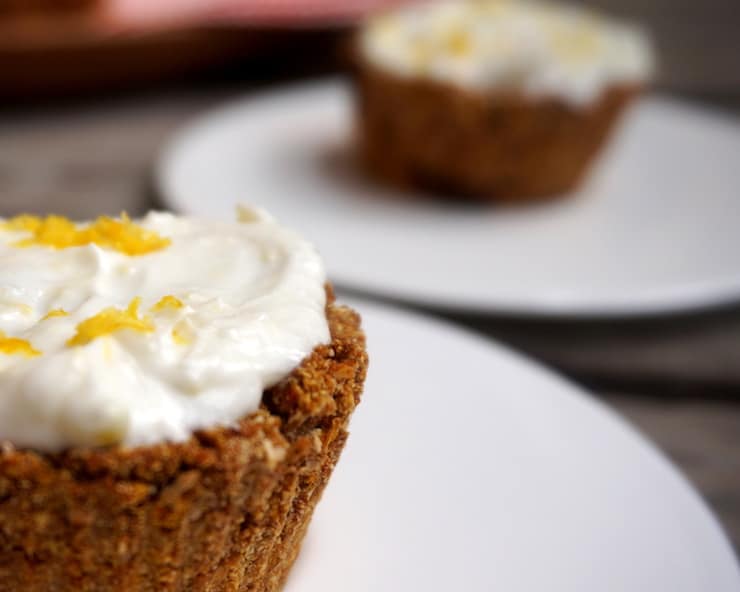 close up of carrot cupcake with white frosting on a white plate