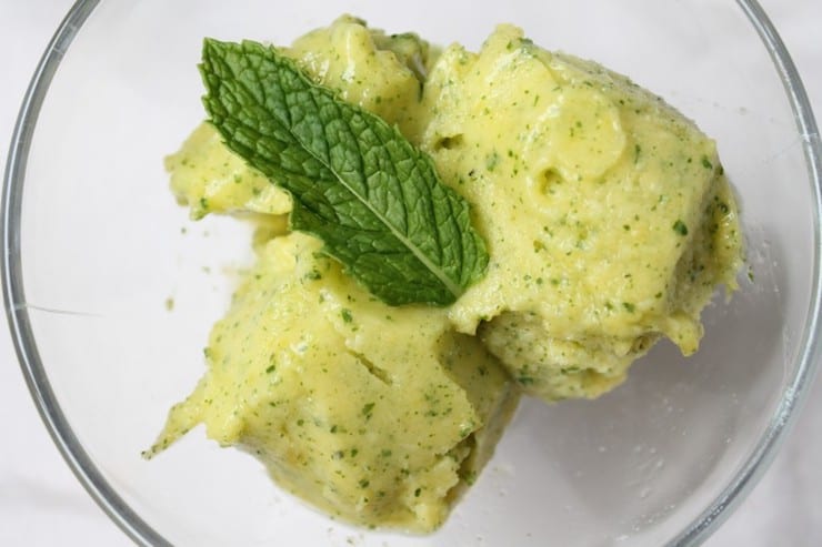 three scoops of yellow pineapple sorbet with green mint flecks in it topped with green mint leaf