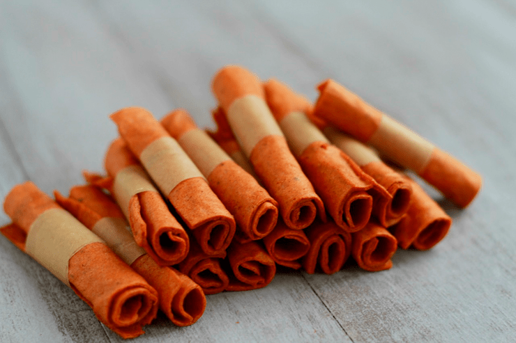 Several rolled up orange fruit leathers on a table