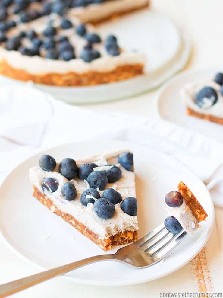 One slice of blueberry tart on a white plate with whole tart in background