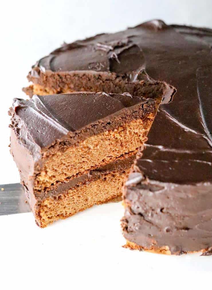 Whole vanilla cake with chocolate frosting with a slice being taken out of it