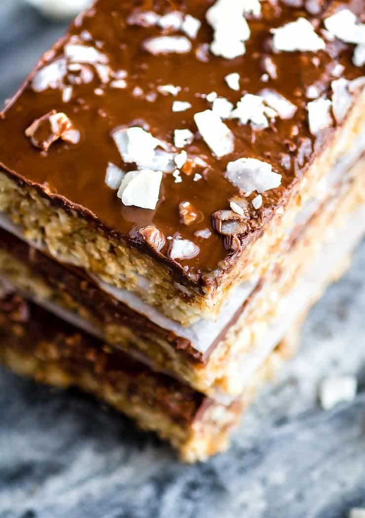 three stacked cashew bars with a layer of chocolate on top sprinkled with coconut