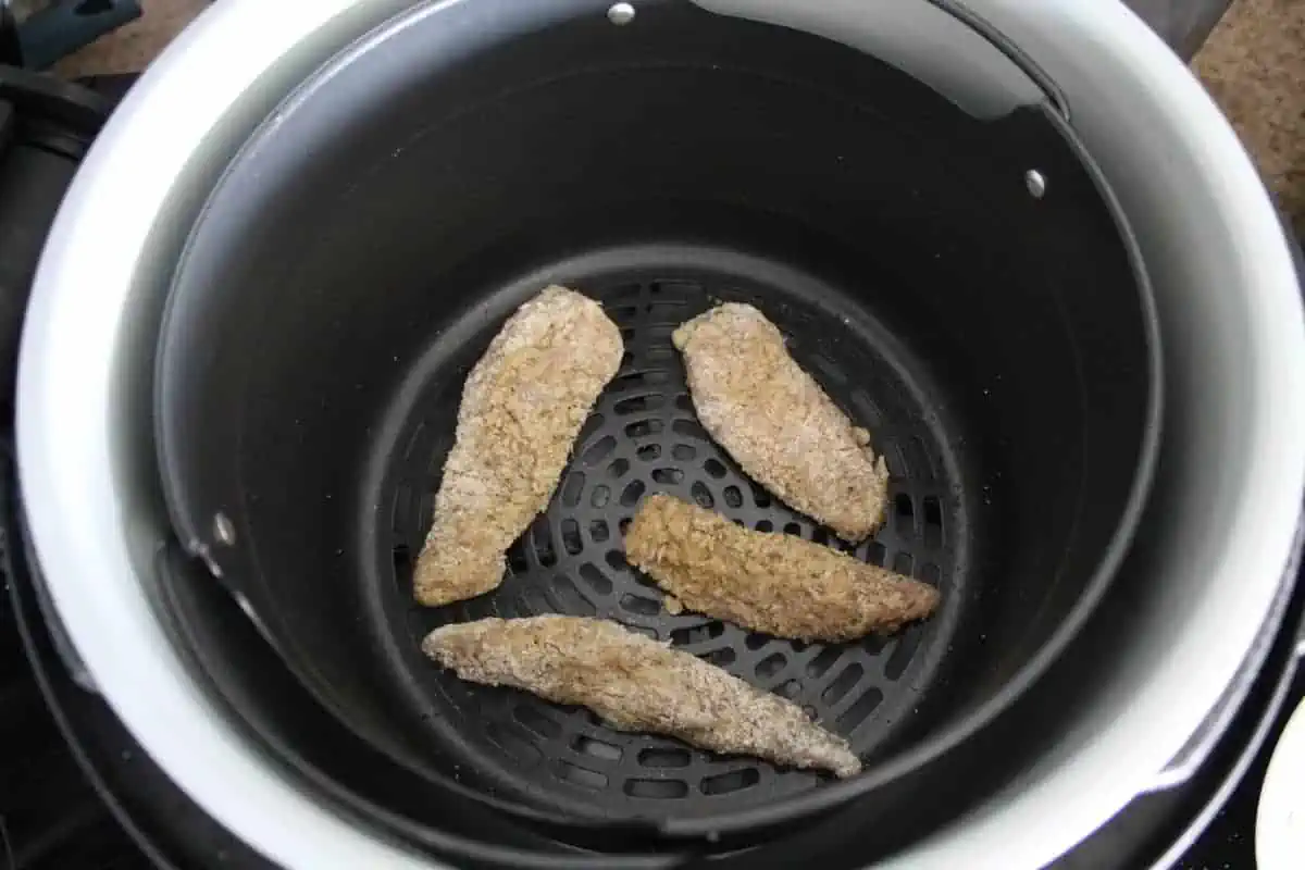 Uncooked chicken fingers in an air fryer basket
