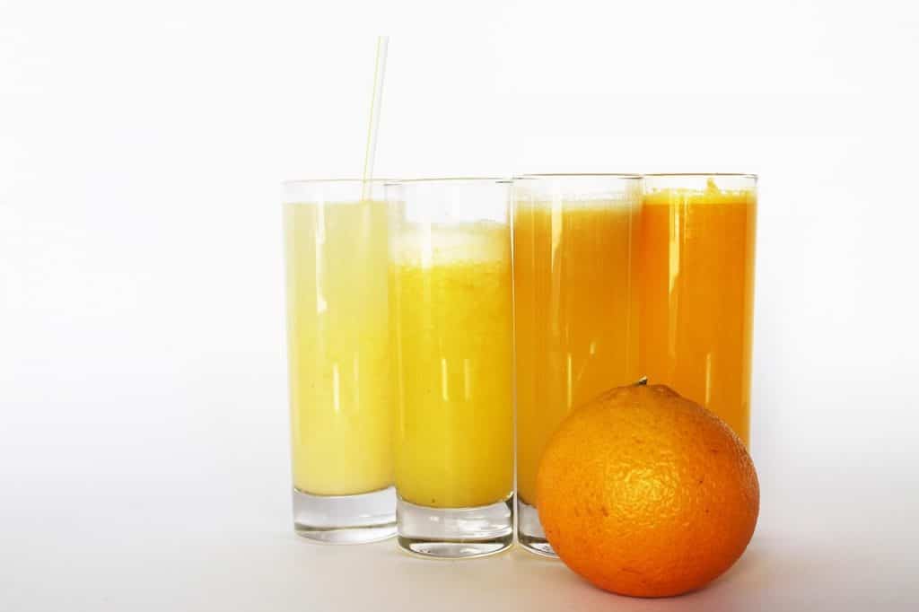 four glasses of orange juice next to an orange