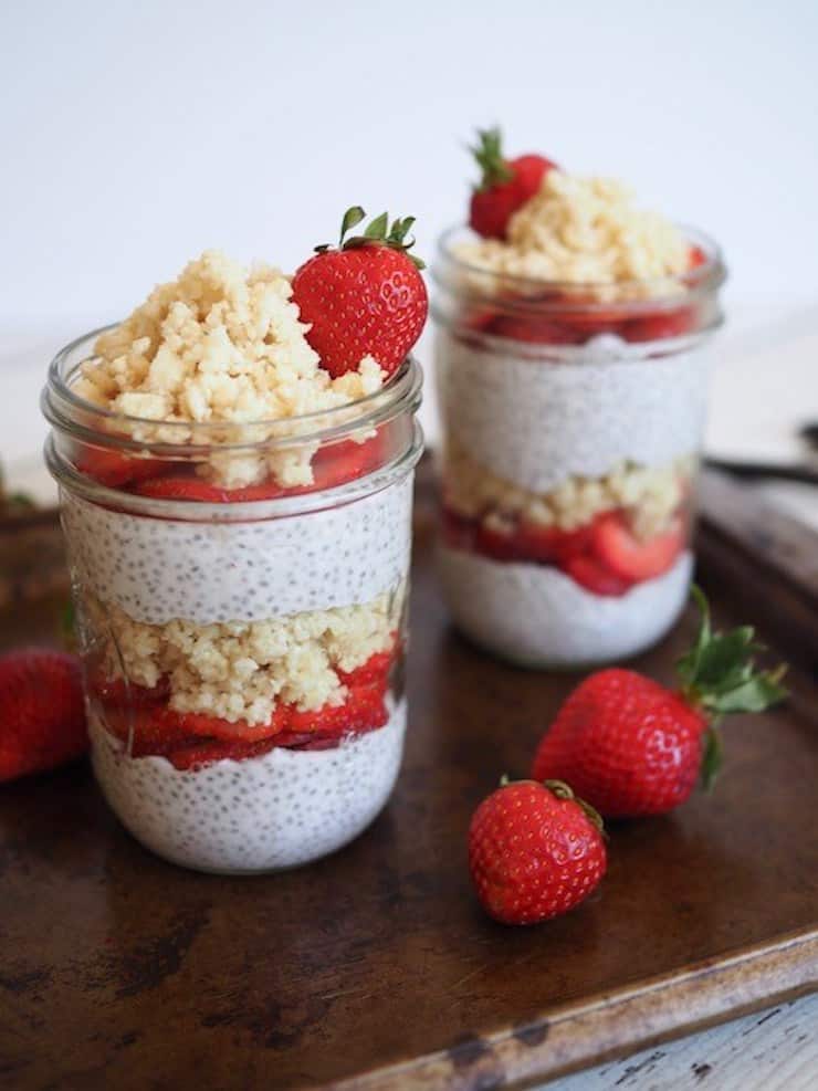 two mason jars with layered parfait of white chia pudding, strawberries and crumbles