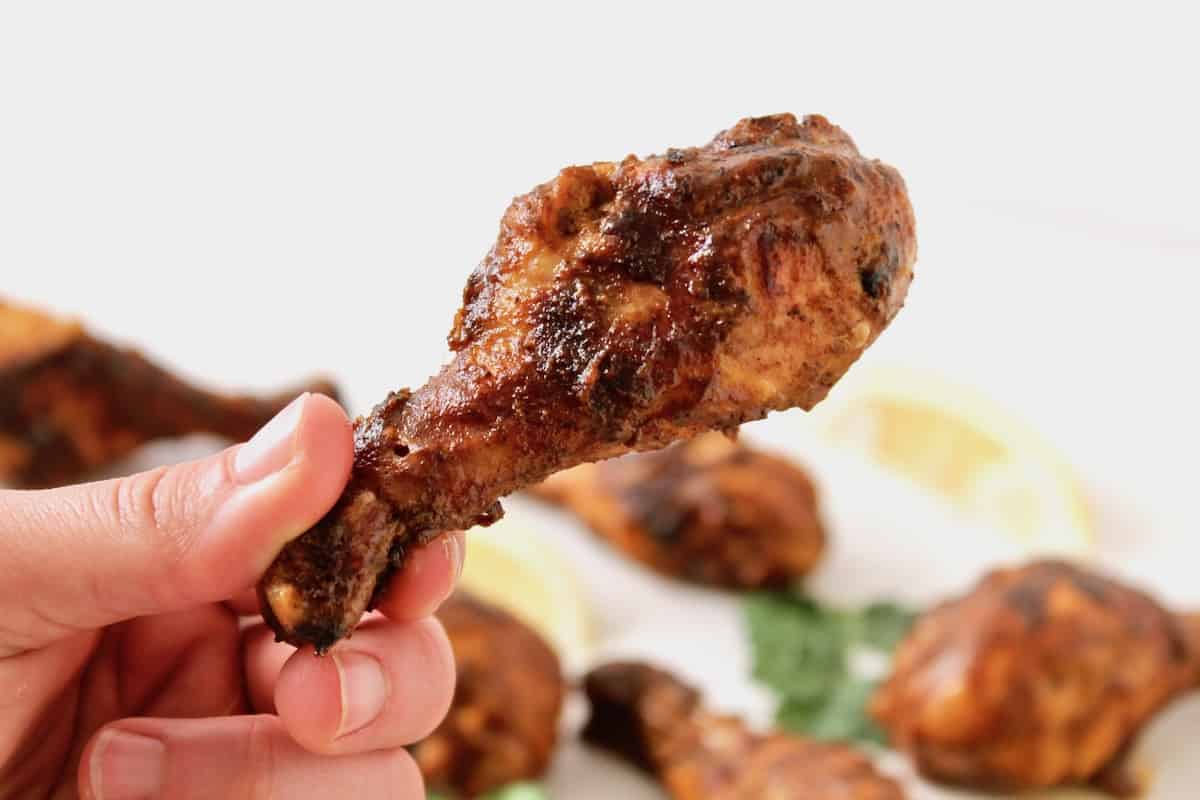 Close up of a hand holding a drumstick of chicken tandoori