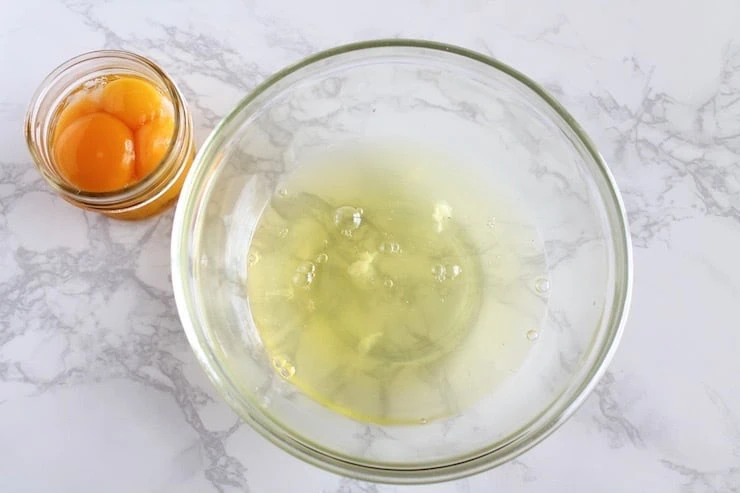 Overhead view of egg whites in clear bowl with egg yolks in container next to it