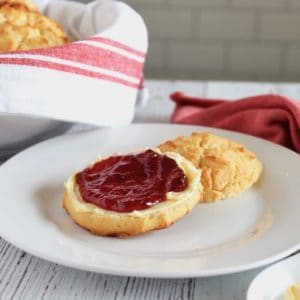 One paleo biscuit cut in half with butter and jam on it on a white plate