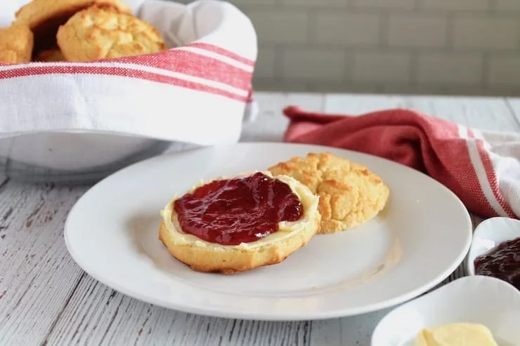 One paleo biscuit cut in half with butter and jam on it on a white plate