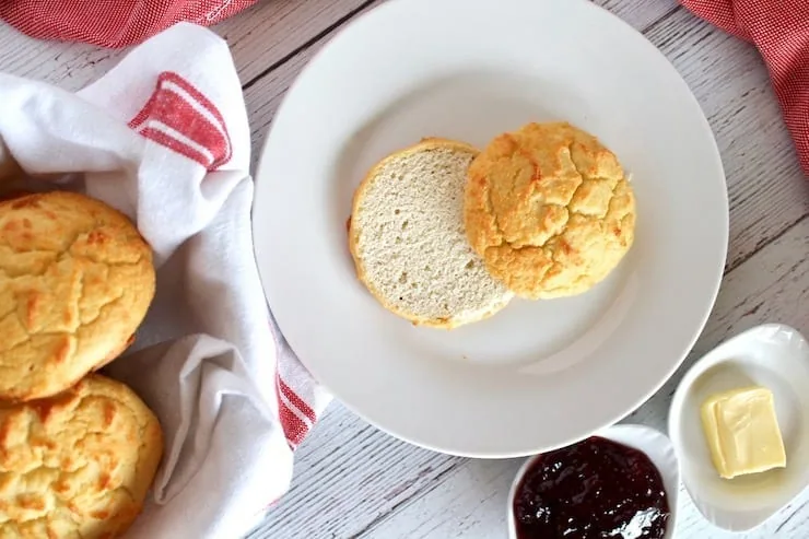 overhead view of one paleo biscuit cut in half on a white plate next to a bowl of biscuits