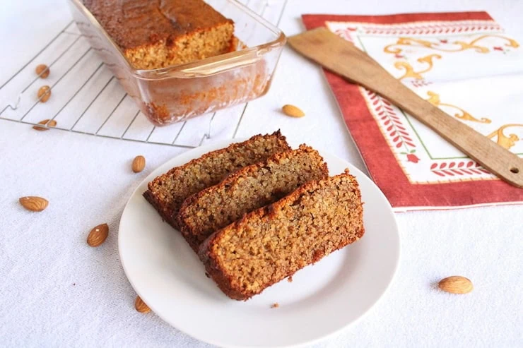 Slices of almond cake ona white plate with a loaf cake in the background