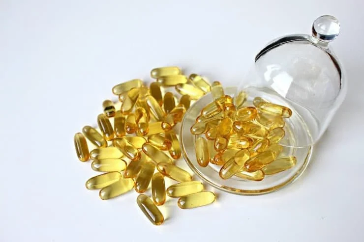 Yellow gel capsules on a clear plate spilling onto a white table
