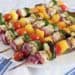 Close up of vegetable and chicken kabobs on wooden skewers on white plate