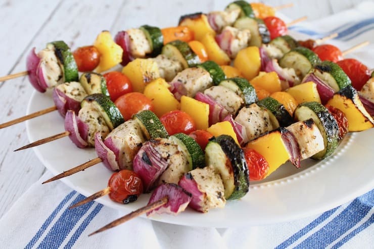 Close up of vegetable and chicken kabobs on wooden skewers on white plate