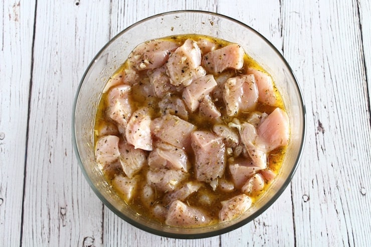 raw cubed chicken in marinade in a clear bowl on a white wooden table
