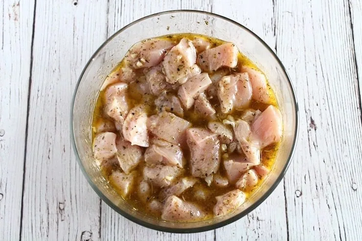 raw cubed chicken in marinade in a clear bowl on a white wooden table