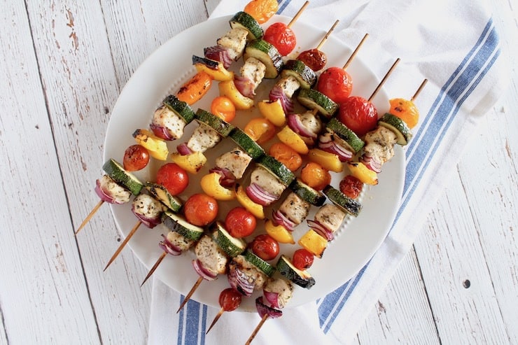 overhead view of cooked chicken kabobs on a white plate with white cloth with blue stripe underneath