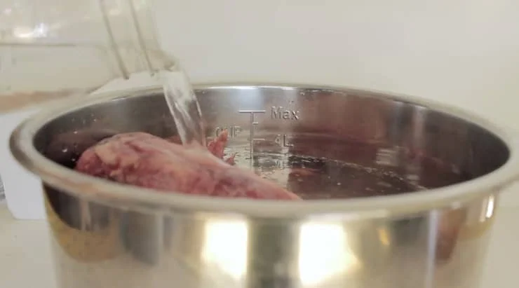 Water being poured into a stainless steel pressure cooker pot with chicken bones inside