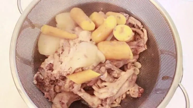Mesh Strainer with chicken bones and carrots in it over a pot