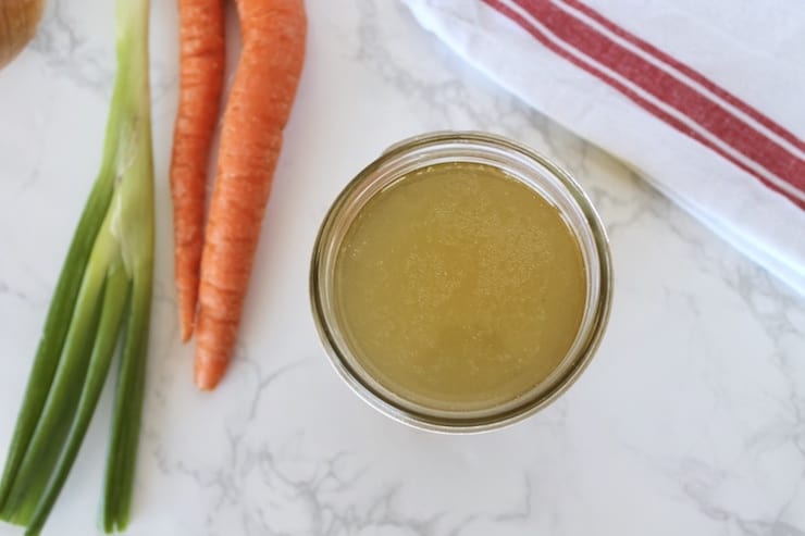 Overhead view of a jar of bone broth with carrots and an onion on the table