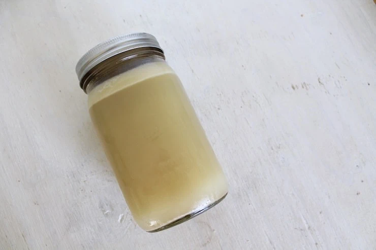 Sealed jar of bone broth with fat layer on top on a white wooden table