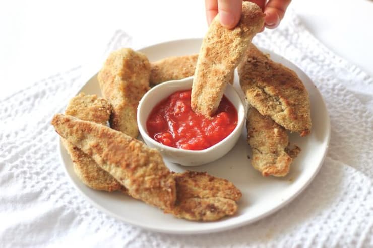 Chicken fingers on a plate with a hand dipping one into tomato sauce