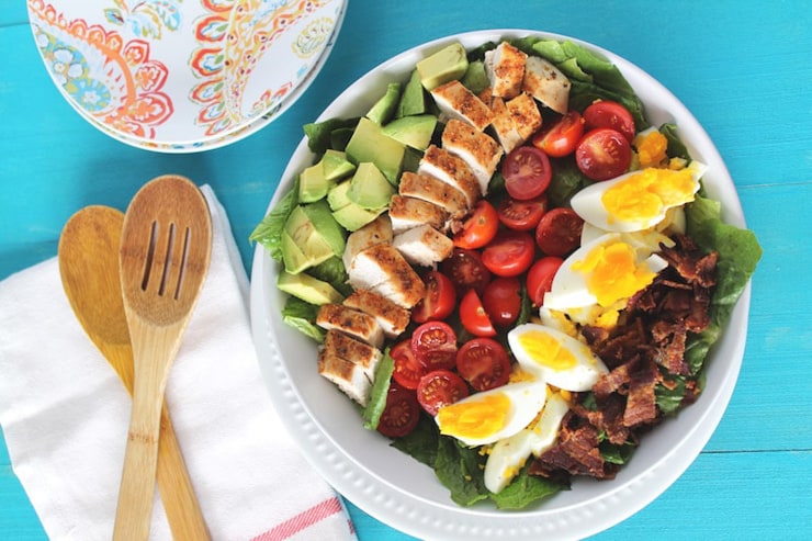 An overhead shot of a cobb salad with salad servers at the side