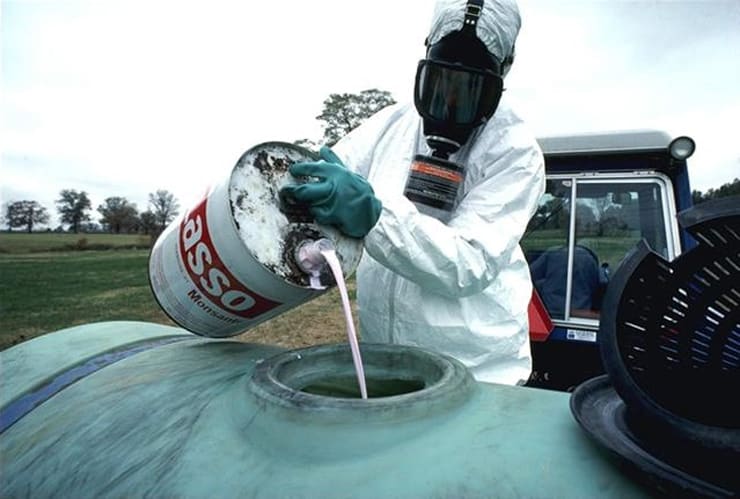 A man wearing a mask and body suit pouring hazzerdous pesticide into a container