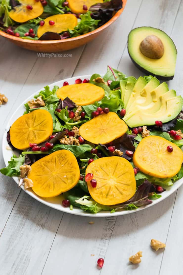A salad on a white plate with persimmons, pomegranate and avocado