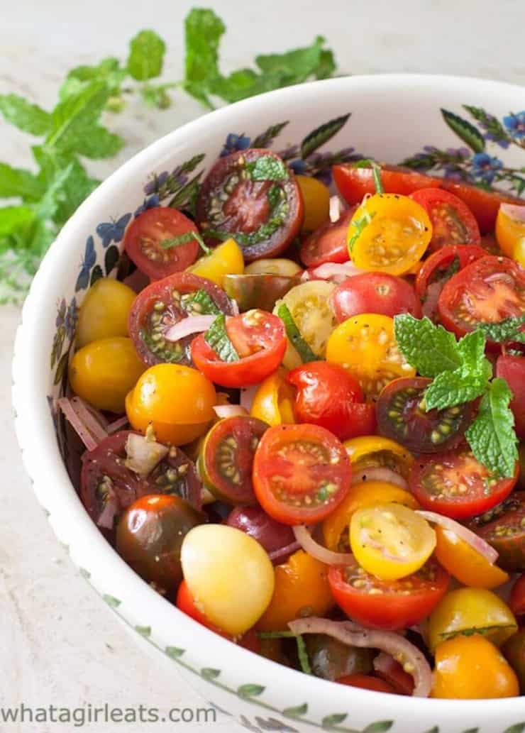 A chopped tomato salad in a white bowl topped with herbs