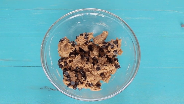 overhead view of dough mixture with chocolate chips in clear bowl on blue wooden table