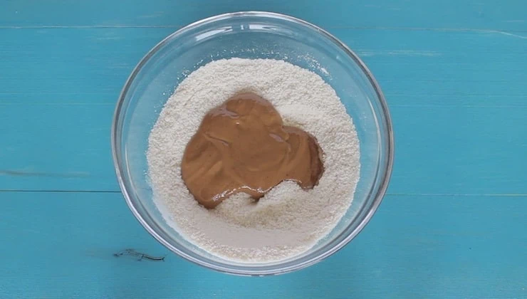 overhead view of dry ingredients with wet ingredients added on top in clear bowl on blue wooden table