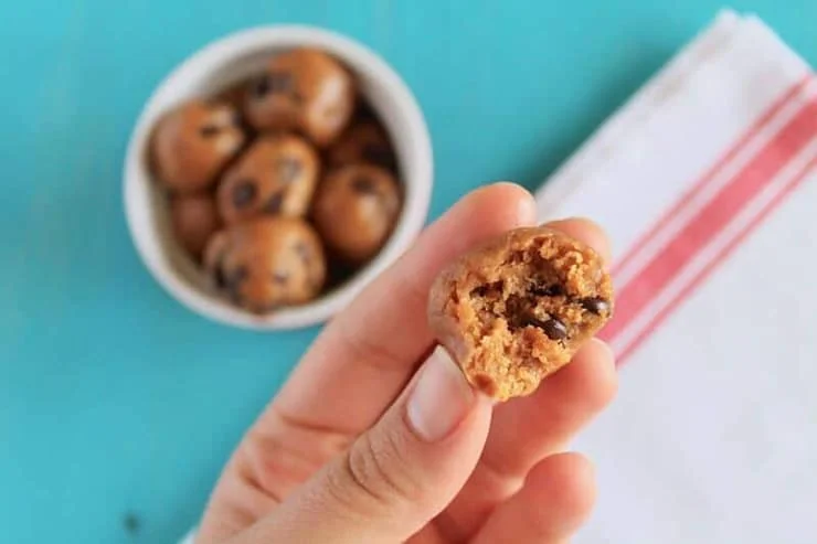 A hand holding a chocolate chip energy ball with a bite out