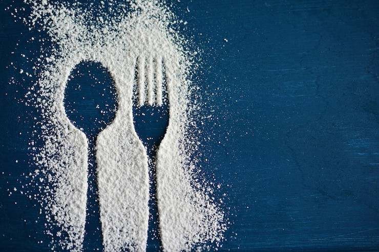 An outline of a spoon and fork dusted with sugar on a blue surface