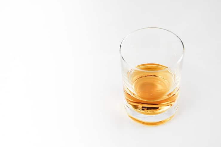 A photo of whiskey in a small glass sitting on a white surface