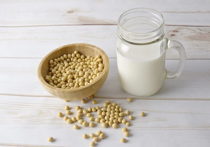 A bowl of soy bean and a jug of milk on a wooden surface