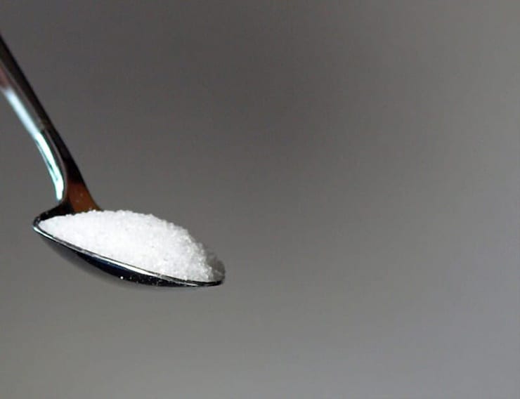 A photo of a teaspoon of sugar with a grey background