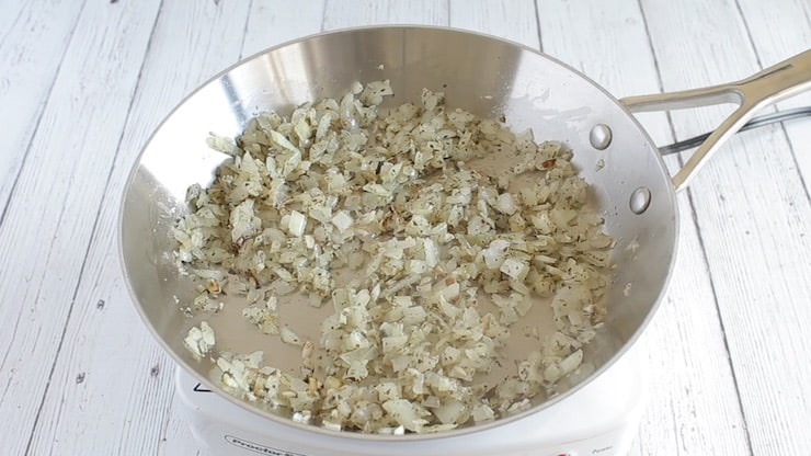 Diced onions and herbs cooking in a stainless steel pan