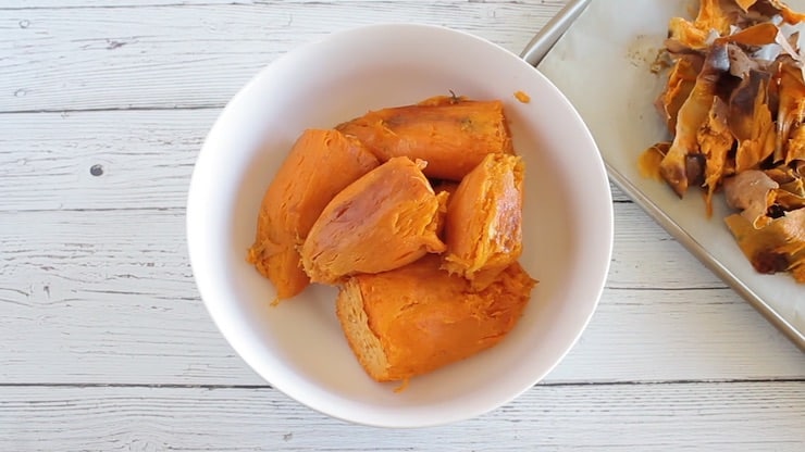 Cooked sweet potato pieces in a white bowl on a white wooden table