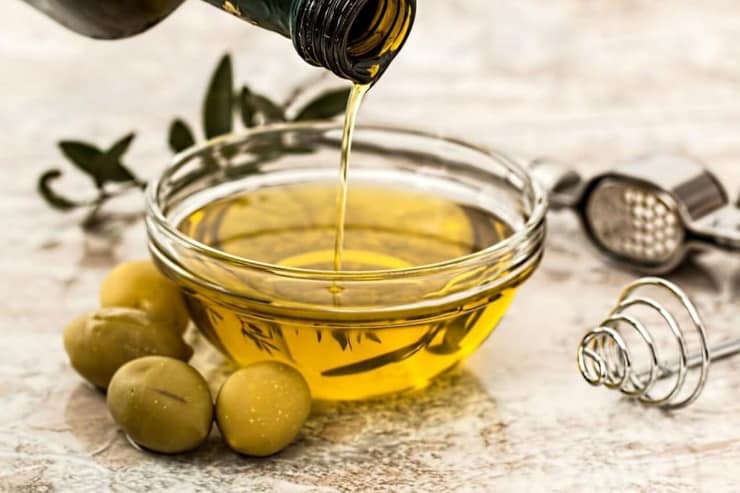 A small glass bowl of olive oil with olives at the side