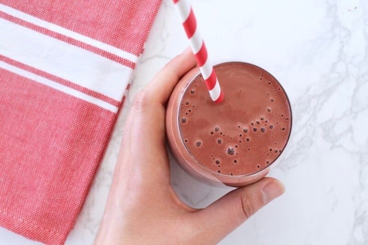 Red smoothie with a red a white striped straw with a hand holding the cup