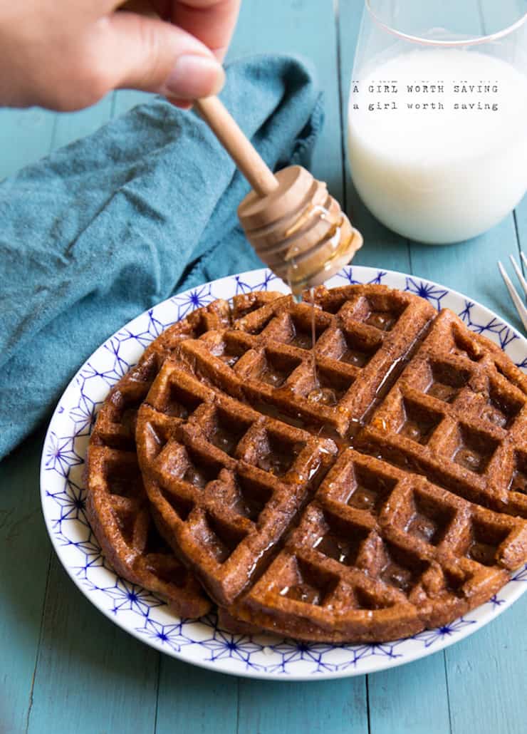 two stacked pumpkin waffles being drizzled with honey on a blue cloth
