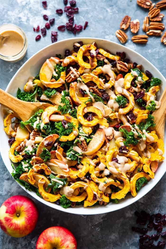 Large white bowl filled with kale and sliced delicata squash salad with a wooden spoon in the salad 